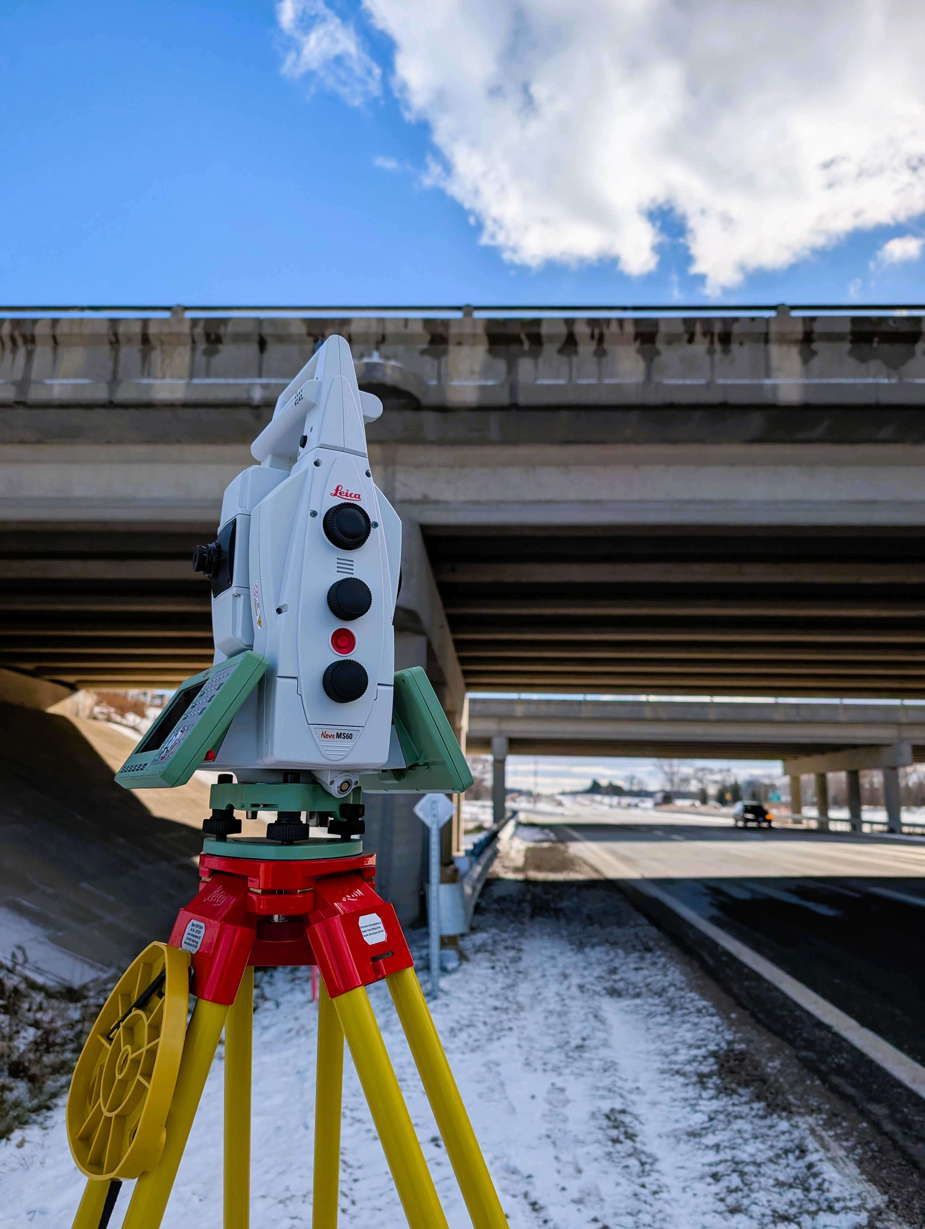 Leica total station set up beneath a highway overpass in winter — Modeland Rd survey project